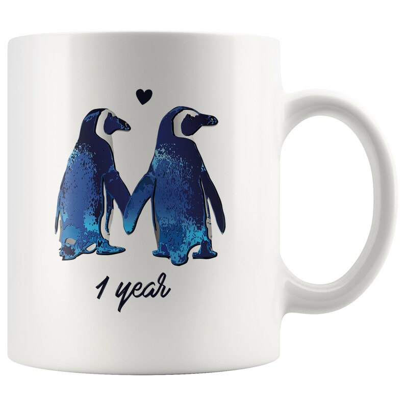 May include: White ceramic mug with a blue and white illustration of two penguins holding hands with a small heart above them. The text "1 year" is printed below the penguins.