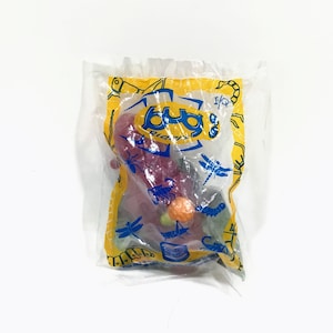May include: A clear plastic bag with a yellow and blue Bug Bitz logo. The bag contains a red, green, and orange plastic toy bug. The bag also has a small sticker that says "1/9".