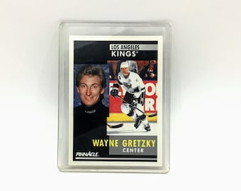 Könnte beinhalten: Eine Pinnacle-Hockeykarte mit Wayne Gretzky, einem Spieler der Los Angeles Kings. Die Karte ist weiß mit schwarzen und gelben Akzenten. Die Karte zeigt ein Foto von Gretzky in seinem Kings-Trikot, das einen Hockeyschläger hält. Die Karte enthält auch den Text "Wayne Gretzky, Center".