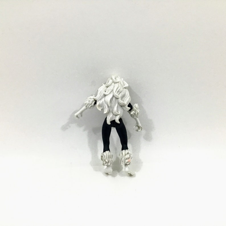 May include: Black and white action figure of a female superhero with long white hair and black fur trim. The figure is wearing a black suit with white fur trim on the boots.