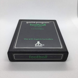 May include: A black Atari game cartridge for the Atari 2600 console. The cartridge is labeled "game program™ football CX-2625 1-3 FOOTBALL" and "ATARIⓇ football".