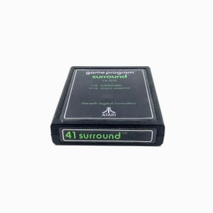 May include: A black Atari game cartridge labeled "41 surround" with the text "game program surround" and "CX-2641". The cartridge also lists "1-12 SURROUND" and "13-14 VIDEO GRAFFITI". The Atari logo is visible.