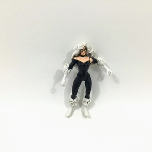 May include: Black Cat action figure with white fur accents. The figure is posed with arms outstretched and has a black catsuit with a white collar.