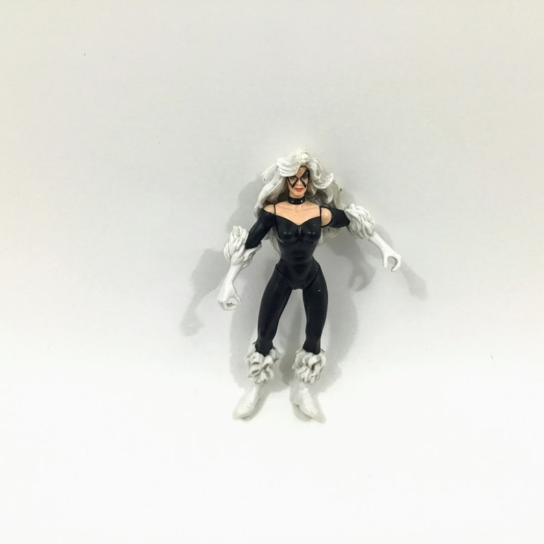 May include: Black Cat action figure with white fur accents. The figure is posed with arms outstretched and has a black catsuit with a white collar.