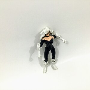May include: Black Cat action figure with white fur, black clothing, and a black mask. The figure is posed with one arm raised and the other arm bent at the elbow.