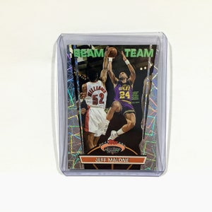 May include: A Topps Stadium Club basketball card featuring Jeff Malone of the Utah Jazz. The card has a holographic background with a green "Beam Team" text at the top. Malone is wearing a purple and gold jersey with the number 24. He is jumping up to shoot the ball. Another player in a red jersey with the number 52 is in the background.