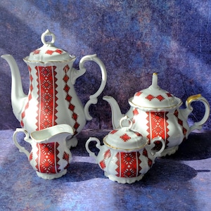 May include: A white porcelain tea set consisting of a tall teapot, a smaller teapot, a lidded sugar bowl, and a creamer. Each piece features a vertical red and black geometric pattern with intricate diamond motifs and gold-trimmed edges.