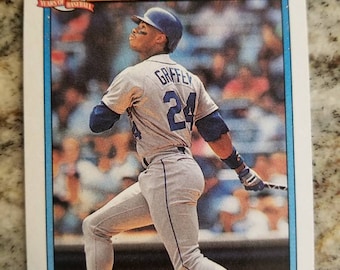 May include: A baseball card featuring Ken Griffey Jr. in a Seattle Mariners uniform. The card is from the 1992 Topps All-Star series. The card has a blue, white, and orange color scheme. The card features a photo of Griffey Jr. swinging a bat. The card also features the text "Topps All-Star American League" and "Ken Griffey, Jr."