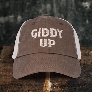May include: A brown and white trucker hat with the text "Giddy Up" embroidered in white on the front.