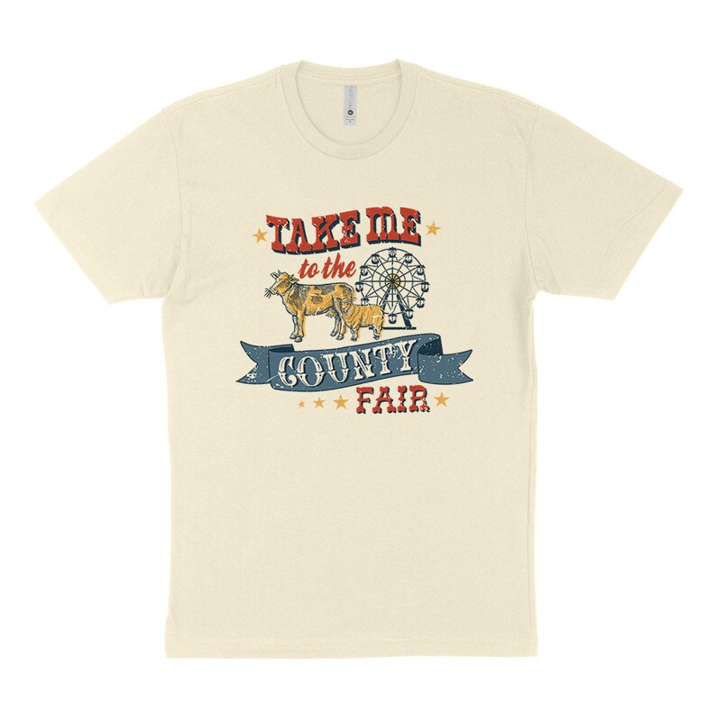 May include: Cream-colored t-shirt featuring a vintage-style graphic. The design includes the text "TAKE ME to the COUNTY FAIR" in red and blue, along with illustrations of a cow, calf, and a Ferris wheel. The shirt has short sleeves.