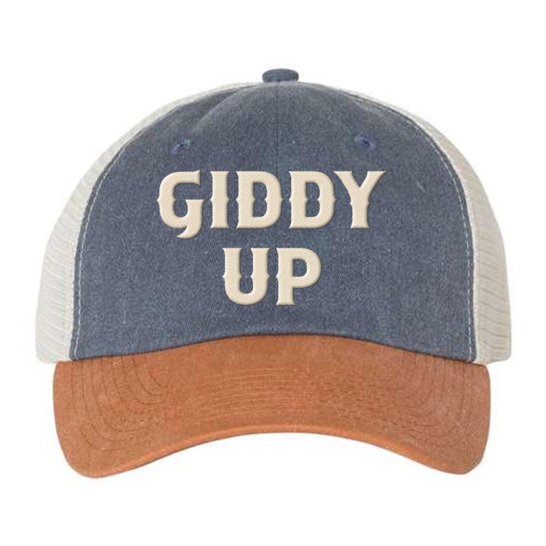 May include: A blue and brown trucker hat with a white mesh back. The hat has the words "Giddy Up" embroidered on the front in a cream color.
