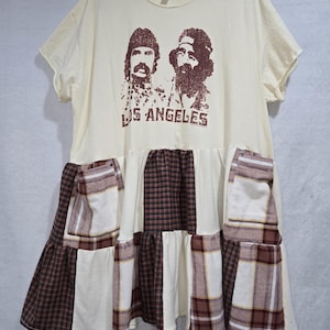 May include: Cream-colored t-shirt dress with a brown graphic of two men and the text "LOS ANGELES." The dress features a patchwork skirt with brown, cream, and plaid panels, creating a unique, layered design.