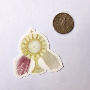 May include: A gold and white sticker of a monstrance with a cross on top and three white and purple tassels. The sticker is about the size of a quarter.