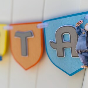 May include: A decorative banner featuring shield-shaped pennants in yellow, orange, and light blue. The pennants display large, raised gray letters. A cartoon cheetah character dressed in a blue police uniform and holding a donut is attached.