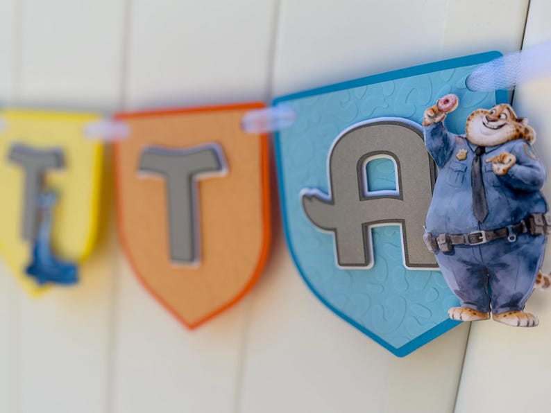 May include: A decorative banner featuring shield-shaped pennants in yellow, orange, and light blue. The pennants display large, raised gray letters. A cartoon cheetah character dressed in a blue police uniform and holding a donut is attached.