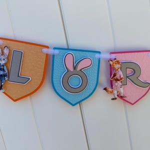 May include: A decorative banner featuring shield-shaped pennants in orange, blue, pink, and green. The pennants display the letters L, O, R, and part of another letter. Characters from Zootopia are attached to the L and R pennants.