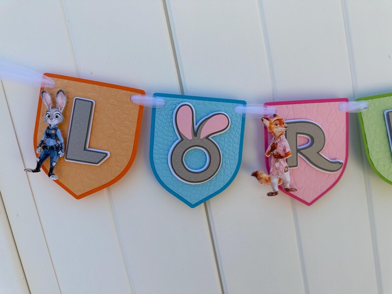 May include: A decorative banner featuring shield-shaped pennants in orange, blue, pink, and green. The pennants display the letters L, O, R, and part of another letter. Characters from Zootopia are attached to the L and R pennants.