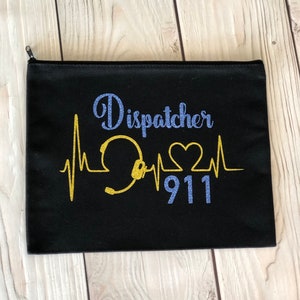 May include: Black zippered pouch with the word "Dispatcher" in blue glitter script, a gold glitter graphic of a headset and heartbeat, and the number "911" in blue glitter. The pouch is rectangular.