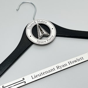 May include: Black wooden hanger with a silver metal United States Space Force logo and a silver metal nameplate that reads "Lieutenant Ryan Howlett".