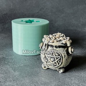 May include: A teal cylindrical mold with a star-shaped cutout next to a small, off-white cauldron-shaped candle. The candle has a pentagram design and is filled with wax. The text "MilovFactoryMoldUA" is visible.