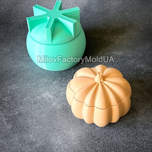 以下が含まれることがあります： 星型の蓋が付いたパンプキン型の装飾箱2つ。パンプキン型の箱は薄い茶色で、もう一方の箱は薄い緑色です。