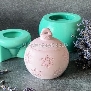 Pu&ograve; includere: Uno stampo per ornamenti natalizi rosa con un motivo a fiocco di neve. Lo stampo &egrave; in silicone e viene mostrato con un ornamento finito.