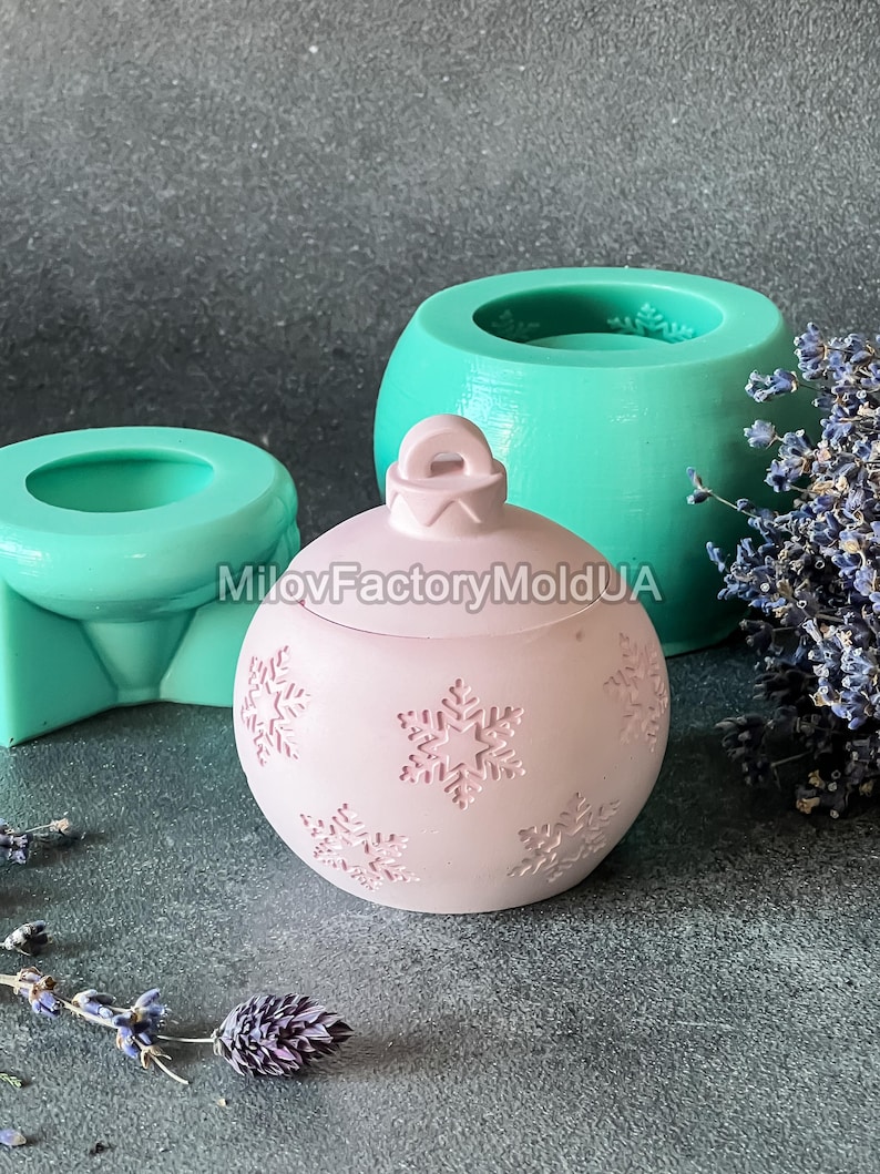 Pu&ograve; includere: Uno stampo per ornamenti natalizi rosa con un motivo a fiocco di neve. Lo stampo &egrave; in silicone e viene mostrato con un ornamento finito.