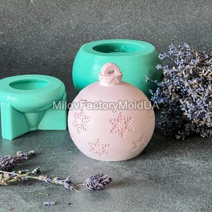Pu&ograve; includere: Uno stampo per ornamenti natalizi rosa con un motivo a fiocco di neve. Lo stampo &egrave; in silicone e viene mostrato con altri due stampi, uno verde e uno blu.