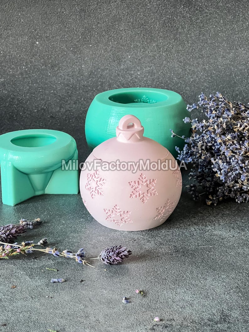Pu&ograve; includere: Uno stampo per ornamenti natalizi rosa con un motivo a fiocco di neve. Lo stampo &egrave; in silicone e viene mostrato con altri due stampi, uno verde e uno blu.