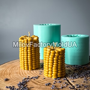 May include: Two yellow corn-shaped candles on a wooden surface with dried lavender flowers. The candles are in silicone molds, one is teal and the other is light blue.