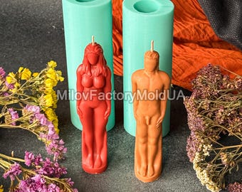 May include: Two figure-shaped candles, one red and one orange, stand in front of two teal candle molds. The red candle depicts a woman, and the orange candle depicts a man. The background includes orange and black fabric, with flowers on either side. The text "MilovFactoryMoldUA" is visible.