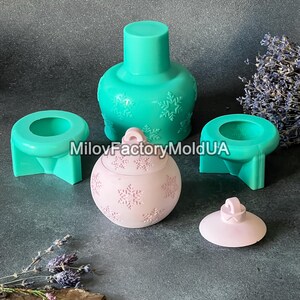 Pu&ograve; includere: Un set di tre stampi in silicone per realizzare decorazioni natalizie. Gli stampi sono verdi e rosa e presentano un motivo a fiocco di neve. Gli stampi sono su una superficie grigia.