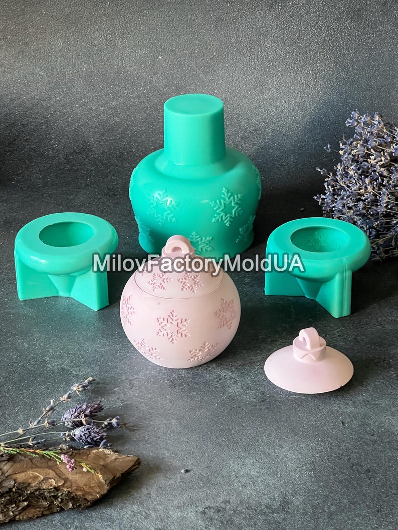 Pu&ograve; includere: Un set di tre stampi in silicone per realizzare decorazioni natalizie. Gli stampi sono verdi e rosa e presentano un motivo a fiocco di neve. Gli stampi sono su una superficie grigia.