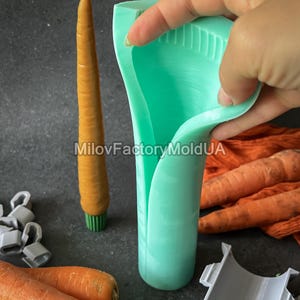 May include: A light green silicone carrot-shaped mould is held in a hand, next to a carrot-shaped candle and fresh carrots. The candle is orange with a green base. The image includes the text "MilovFactoryMoldUA".