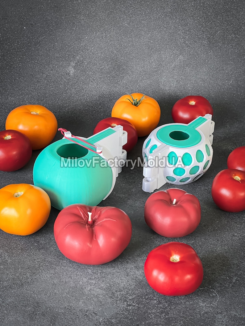 May include: Two 3D printed molds for making tomato-shaped candles. The molds are white and teal blue with a hole in the top. There are several red and orange tomatoes surrounding the molds.