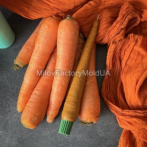 May include: Several fresh, orange carrots with green tops are arranged with a carrot-shaped candle with a green brush base. An orange fabric is draped in the background. The text "MilovFactoryMoldUA" is visible.