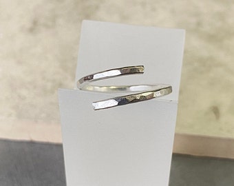 May include: A silver hammered wrap ring with a simple design. The ring is made of a single piece of metal that is wrapped around the finger.