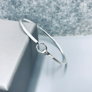 以下が含まれることがあります： ハンマー仕上げと円形の留め具が付いたシルバーのバングルブレスレットです。