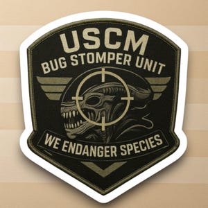 May include: A black and green patch with the text "USCM BUG STOMPER UNIT" and "WE ENDANGER SPECIES". The patch features an alien head within a crosshair, with wings on either side. The patch has a white border.