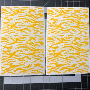 Pode incluir: Duas folhas de estêncil de camuflagem de listras de tigre amarelas. O estêncil é feito de um material fino e flexível e é projetado para ser usado com tinta spray.