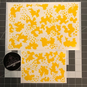 Könnte beinhalten: Zwei Blätter aus gelbem Vinyl-Schablonenmaterial mit einem Tarnmuster. Die Schablone ist für die Verwendung mit Sprühfarbe konzipiert.