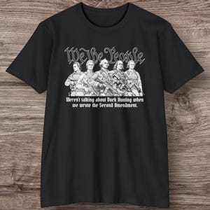Puede incluir: Camiseta negra con un gráfico de cinco figuras armadas y el texto "We the People". Debajo de las figuras está el texto: "Weren't talking about Duck Hunting when we wrote the Second Amendment."