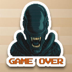 May include: A sticker featuring a pixelated image of an alien creature with an open mouth and sharp teeth. The text "GAME OVER" is displayed in orange block letters below the alien.