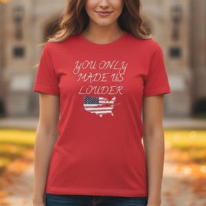 Könnte beinhalten: Rotes T-Shirt mit dem weißen Schriftzug "you only made us louder". Darunter befindet sich eine Grafik der Vereinigten Staaten mit dem Design der amerikanischen Flagge. Das Shirt hat kurze Ärmel.