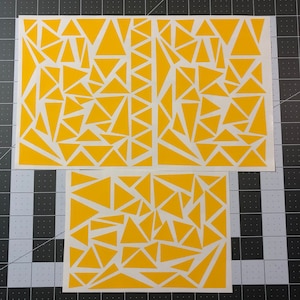 May include: Three sheets of yellow vinyl stencil with a geometric pattern of triangles. The stencils are designed for use with paint or other mediums to create a unique design on a surface.