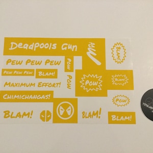 May include: Yellow vinyl stencil sheet with various phrases and images related to the superhero Deadpool. The phrases include "Deadpools Gun", "Pew Pew Pew", "Blam!" and "Maximum Effort!" The images include a stylized Deadpool mask and a speech bubble with the word "Pow!"