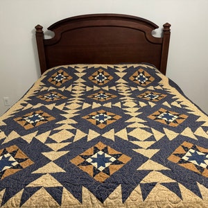 May include: A blue and brown quilt with a star pattern is on a bed with a wooden headboard.