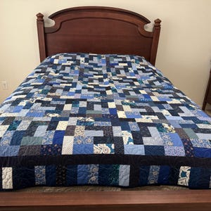 May include: A blue and white patchwork quilt with a dark blue border, laid out on a wooden bed frame.
