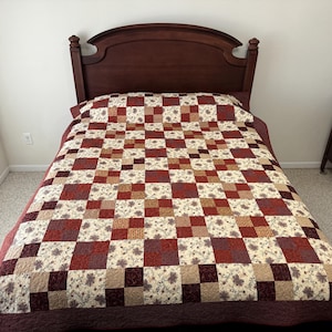 May include: A red and cream patchwork quilt with a floral pattern on a wooden bed frame.