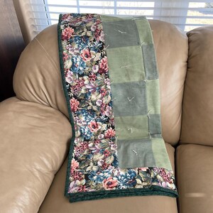 May include: A floral quilt with a green border and a patchwork design. The quilt features a vibrant floral pattern with pink, blue, and purple flowers on a black background. The other side has a green patchwork design.